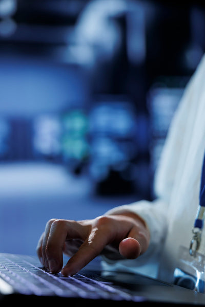 Main d’un ingénieur en cybersécurité travaillant sur un ordinateur portable dans une salle de serveurs, symbolisant la protection et la gestion des systèmes informatiques.